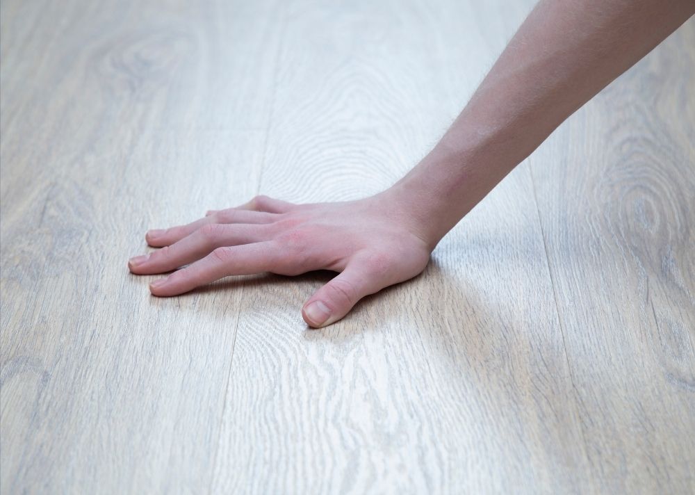 Primer plano de una mano humana probando la temperatura de un suelo laminado de madera clara antes de que una mascota camine sobre él para asegurar su seguridad.